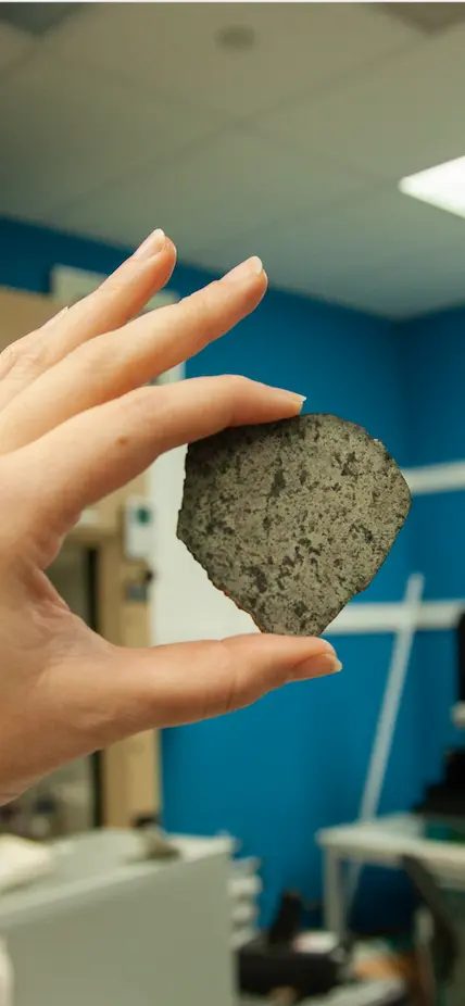 Katy Cain carefully holds Andrew Steele's sample (courtesy of David Blake) of the meteorite SAU 008. A sample of the same meteorite has now traveled back to Mars as a part of the calibration target for the SHERLOC spectrometer onboard the Perseverance rover. Image courtesy Carnegie Institution for Science/Katy Cain