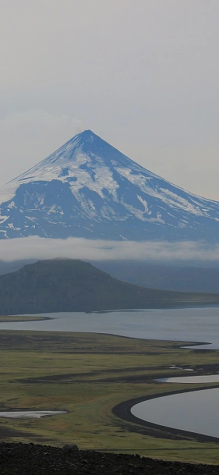 A view over Fisher Caldera in the foreground, looking out to Shishaldin Volcano, at a distance in 2015. The gray and gloomy tone of the photo is characteristic of the weather in the Aleutian Island. Photo is courtesy of Daniel Rasmussen of the National Museum of Natural History. Photo taken under Alaska Maritime National Wildlife Refuge Research and Monitoring Special Use Permit #74500-15-011.