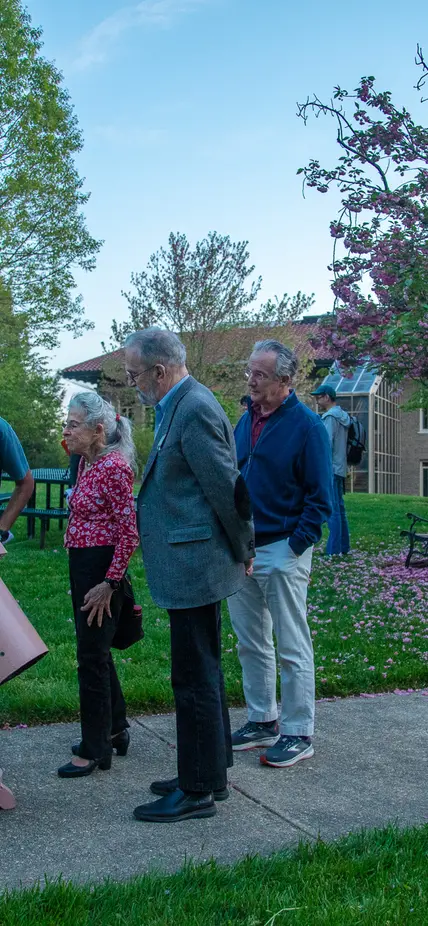 Scientists and members of the public peer through a pastel pink telescope. 