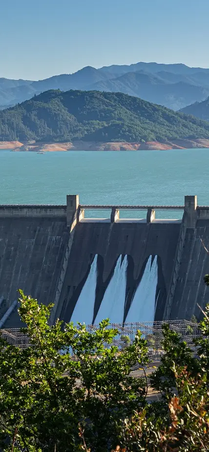 Shasta Dam in Northern California as seen from a distance. Mountains are green in the background. 