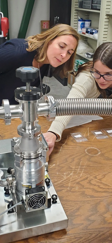 Postdoc Maren Cosens shows a visitor a workstation in the Observatories Machine Shop assembly area.