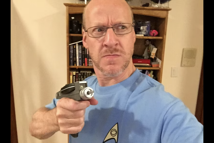Phil Plait holds a face phaser gun while wearing a Star Trek shirt. 