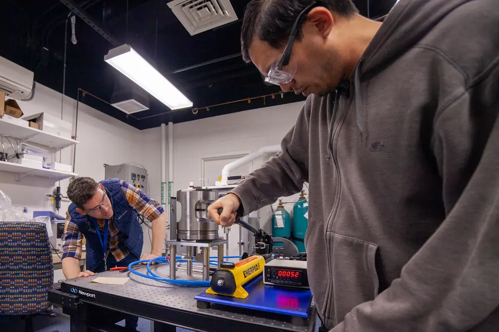 Joseph Lai uses a hand pump to presurize the copper sample. A screen indicates that the sample is under 52 bars of pressure. 