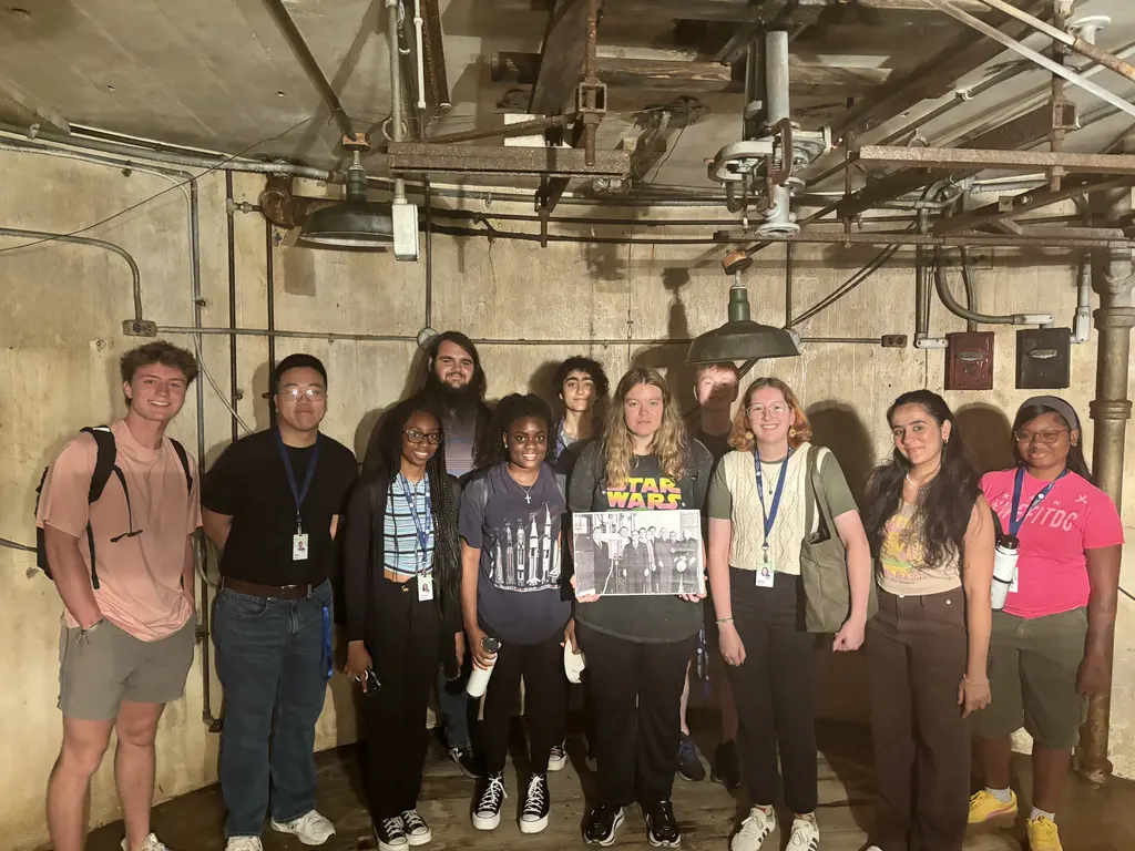 A group of 2024 interns stands in beneath the Atomic Physics Observatory