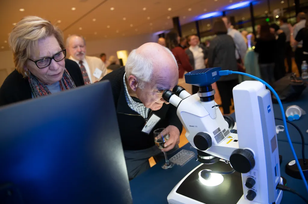 Carolyn and David Gambrel look through a microscope at a Donor Appreciation Event held after a Capital Science Evening lecture by Dr. Margaret McFall-Ngai