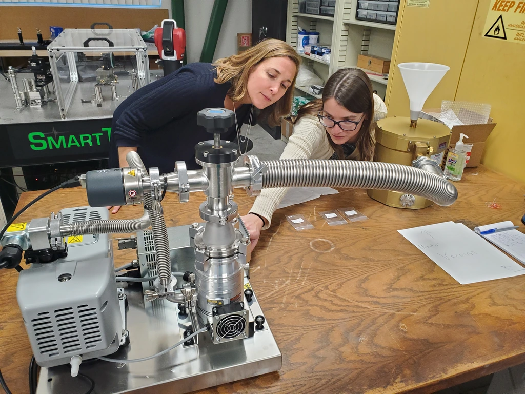 Postdoc Maren Cosens shows a visitor a workstation in the Observatories Machine Shop assembly area.