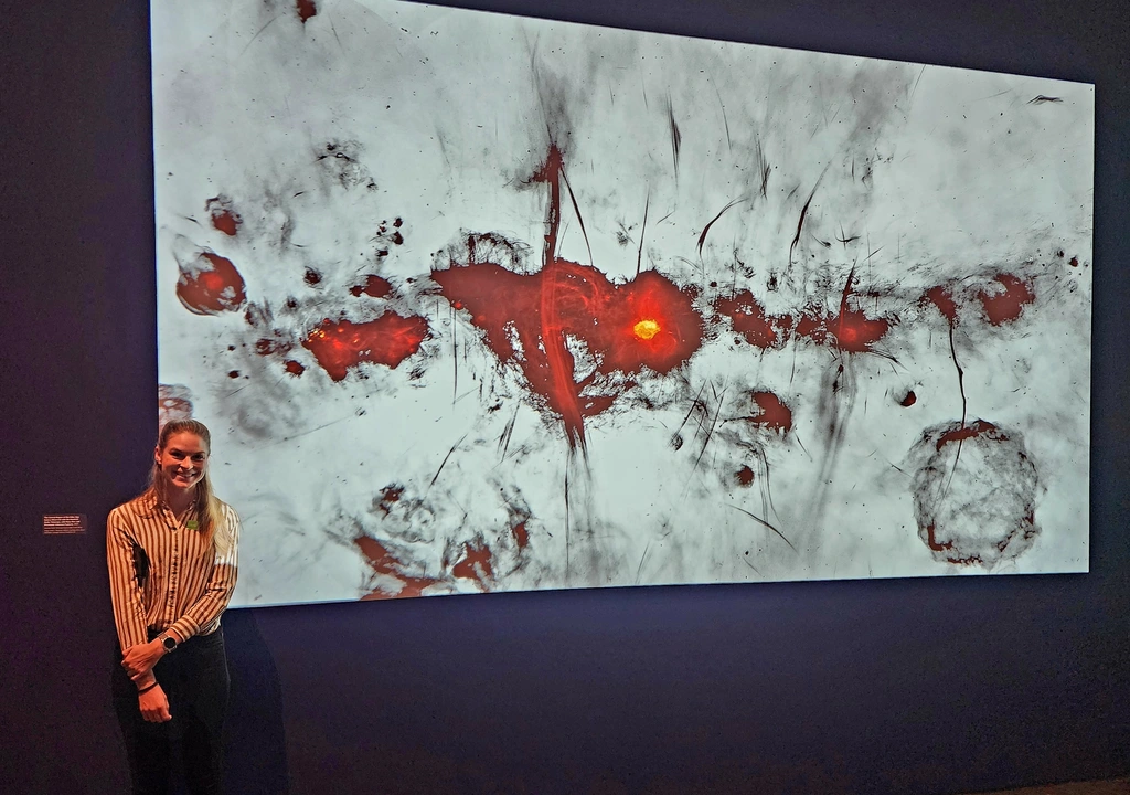 Allison Matthews poses with an image of the Milky Way’s central region captured from the MeerKAT radio telescope and on display in the Los Angeles County Museum of Art’s exhibit Mapping the Infinite: Cosmologies Across Cultures.