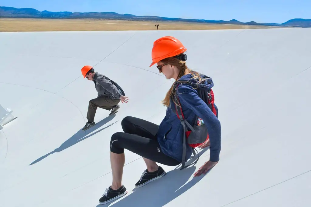 Allison Matthews slides down the side of one of the antennae in the Very Large Array.