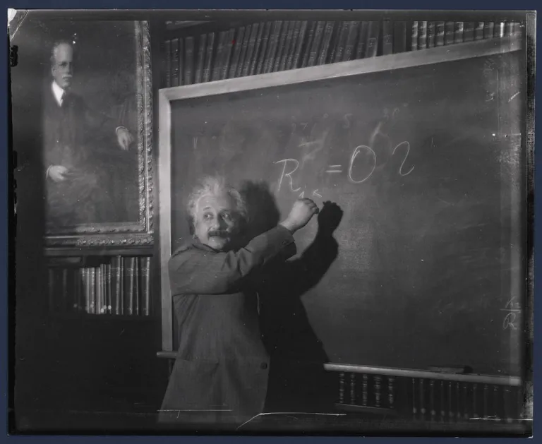 Albert Einstein writes on a chalkboard at the Carnegie Science Observatories with Ellery Hale's portrait in the background. 