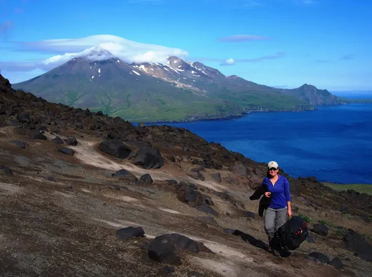 Carnegie’s Diana Roman on the flank of the Cleveland Volcano in 2016. She was dropped off near this location by helicopter, carrying everything she needed to survive for a few days in the Aleutian Islands. Tana Volcano on Chuginadak Island is visible in the background. Creator Anna Barth