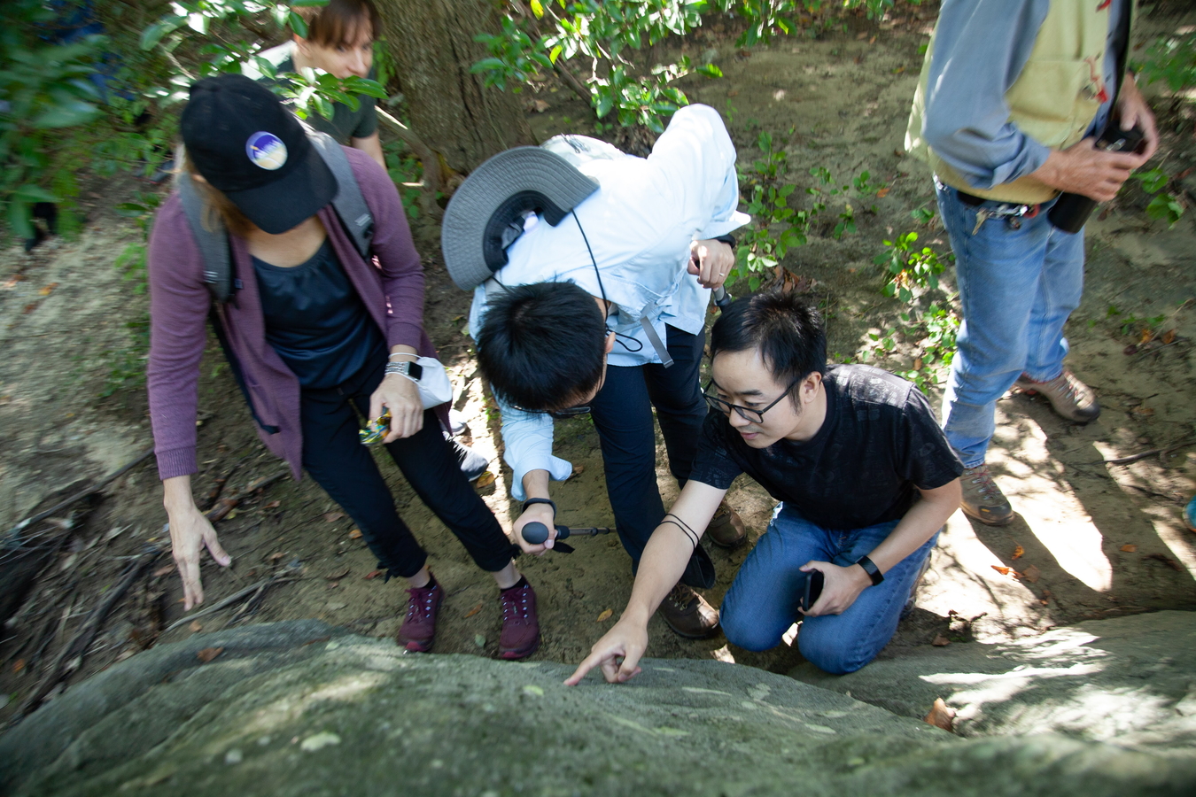 Three postdocs point at a feature in a rock in Rock Creek Park