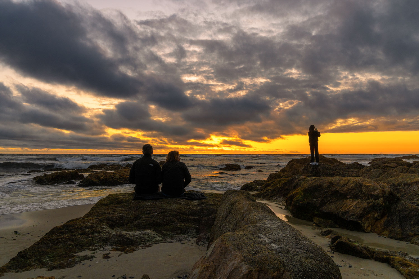 People sit on the shore at sunset. 