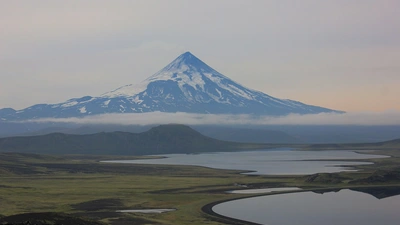 A view over Fisher Caldera in the foreground, looking out to Shishaldin Volcano, at a distance in 2015. The gray and gloomy tone of the photo is characteristic of the weather in the Aleutian Island. Photo is courtesy of Daniel Rasmussen of the National Museum of Natural History. Photo taken under Alaska Maritime National Wildlife Refuge Research and Monitoring Special Use Permit #74500-15-011.