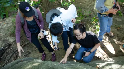 Three postdocs point at a feature in a rock in Rock Creek Park