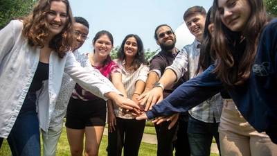 The 2023 summer interns hold their hands in the middle of the circle