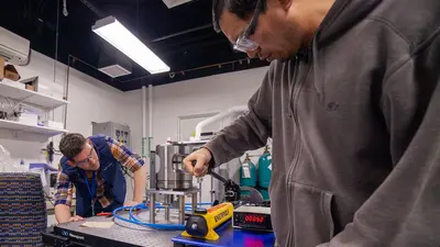 Joseph Lai uses a hand pump to presurize the copper sample. A screen indicates that the sample is under 52 bars of pressure. 