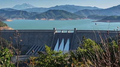 Shasta Dam in Northern California as seen from a distance. Mountains are green in the background. 