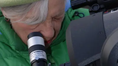 Maxine Singer looks through a telescope during an outreach activity. 