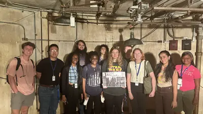 A group of 2024 interns stands in beneath the Atomic Physics Observatory