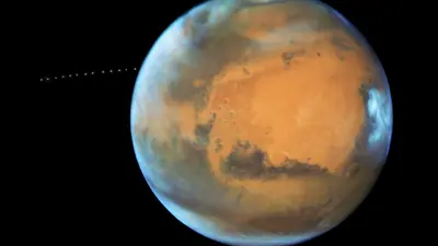 While photographing Mars, NASA’s Hubble Space Telescope captured a cameo appearance of the tiny moon Phobos on its trek around the Red Planet.