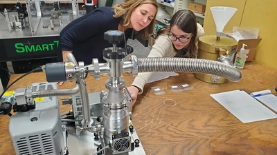Postdoc Maren Cosens shows a visitor a workstation in the Observatories Machine Shop assembly area.