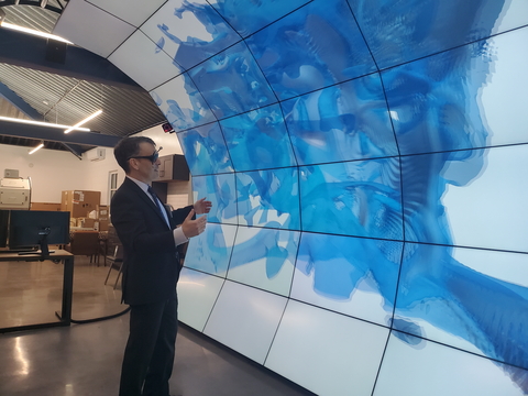 A person stands in front of an immersive visualization display system with 35 2D- and 3D-capable flat panels in the shape of a cresting wave