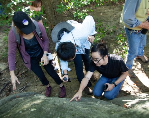Three postdocs point at a feature in a rock in Rock Creek Park
