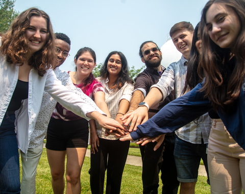 The 2023 summer interns hold their hands in the middle of the circle