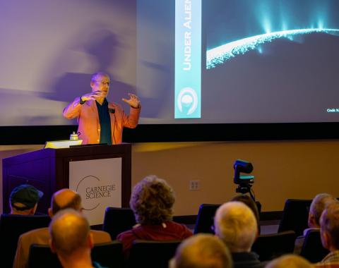 Phil Plait holds his hands up illustrating the pressures that led to Enceladus' fissues