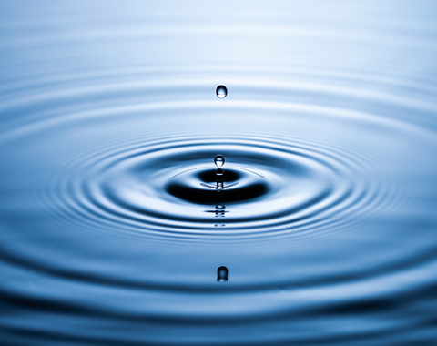 Water droplet ripples outward in blue water