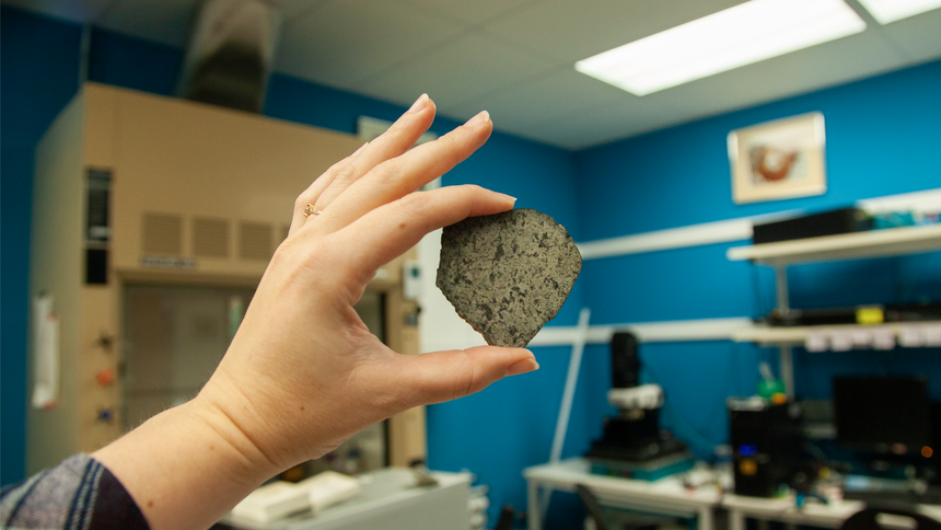 Katy Cain carefully holds Andrew Steele's sample (courtesy of David Blake) of the meteorite SAU 008. A sample of the same meteorite has now traveled back to Mars as a part of the calibration target for the SHERLOC spectrometer onboard the Perseverance rover. Image courtesy Carnegie Institution for Science/Katy Cain