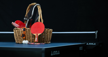 The ping pong table on a black background with a basket of supplies sitting on top. 