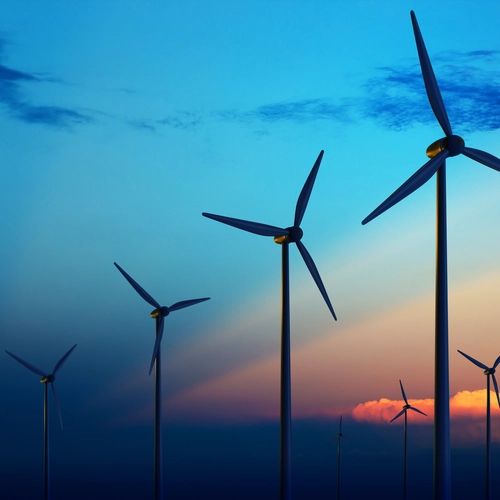 Three windmills at dusk with rays of sunlight across the sky and white fluffy clouds