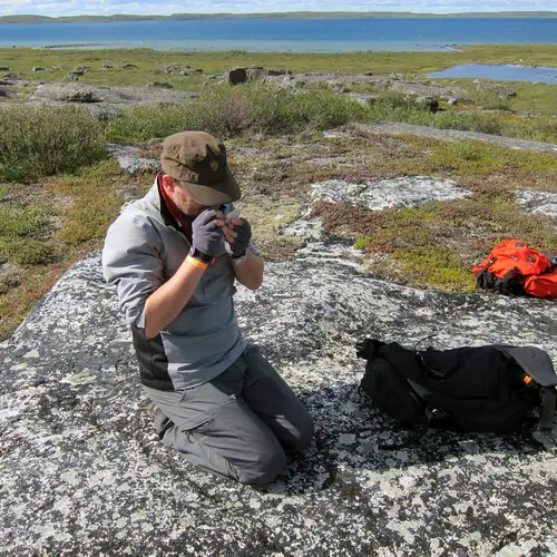 Graham Pearson using on of the field geologist's main tools, a simple hand lens, to look at the mineralogy of a rock during fieldwork at the Slave Craton, Canada.