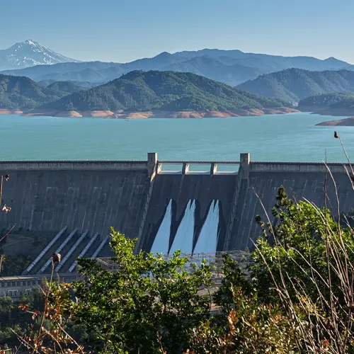 Shasta Dam in Northern California as seen from a distance. Mountains are green in the background.
