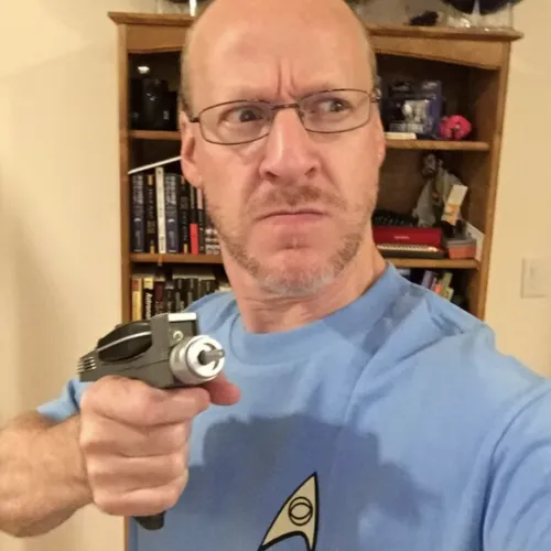 Phil Plait holds a face phaser gun while wearing a Star Trek shirt. 